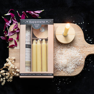 Lifestyle image of happiness bath kit, gift box contains candles, candle holder and bath salts, presented in a beautiful gift box. The image includes a display board and flower petals.