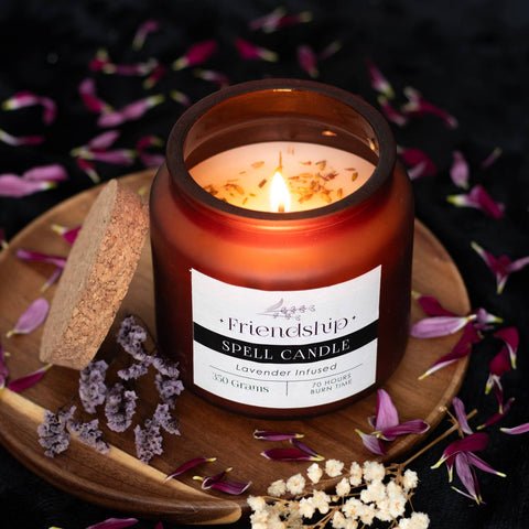 Lifestyle image of a lavender candle in a decorative jar with a cork lid, candle is placed on a wooden board scattered with flower petals.